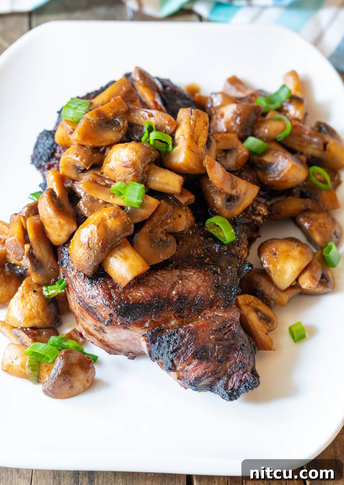 Stir-fried Asian-style mushrooms served over a steak on a white plate. 