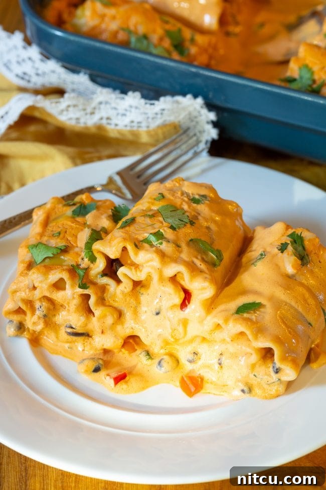 Three perfectly baked Southwest chicken lasagna roll ups on a white plate with a silver fork, ready to eat.