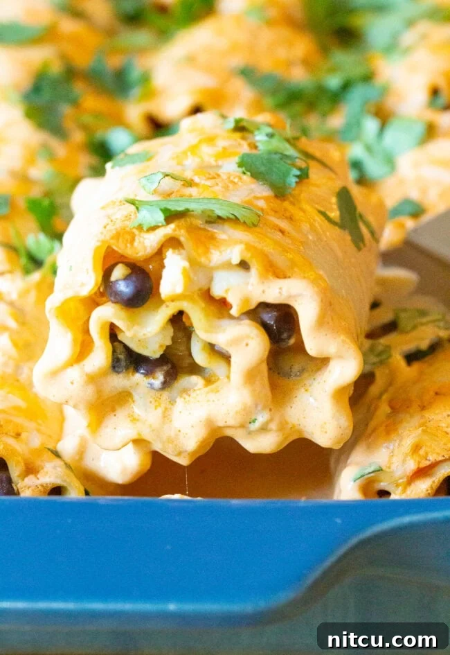 A spatula lifting a southwest lasagna roll up from a blue baking dish, showing the cheesy filling.