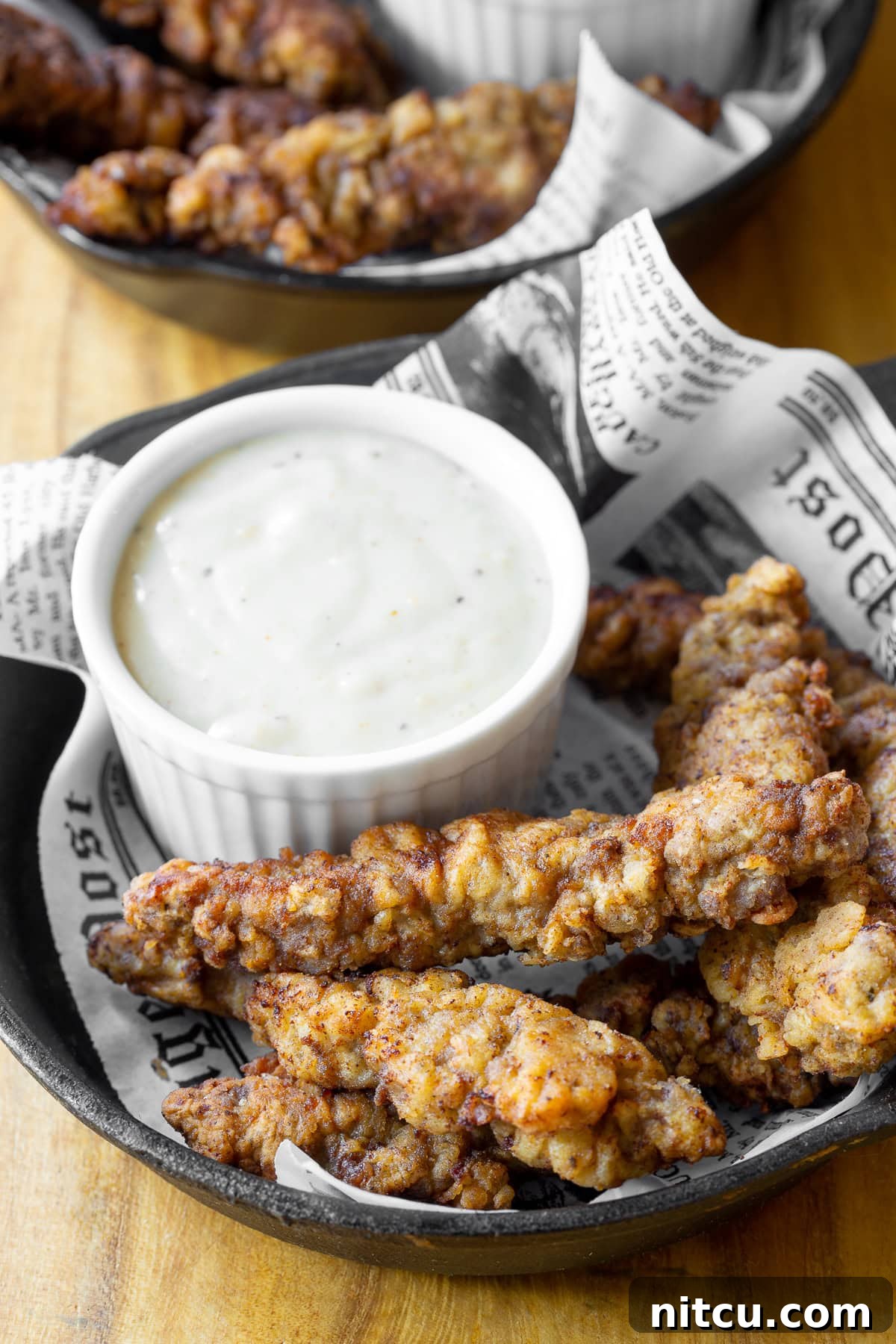 Crispy steak fingers served in a cast iron plate with a side of creamy country gravy for dipping.