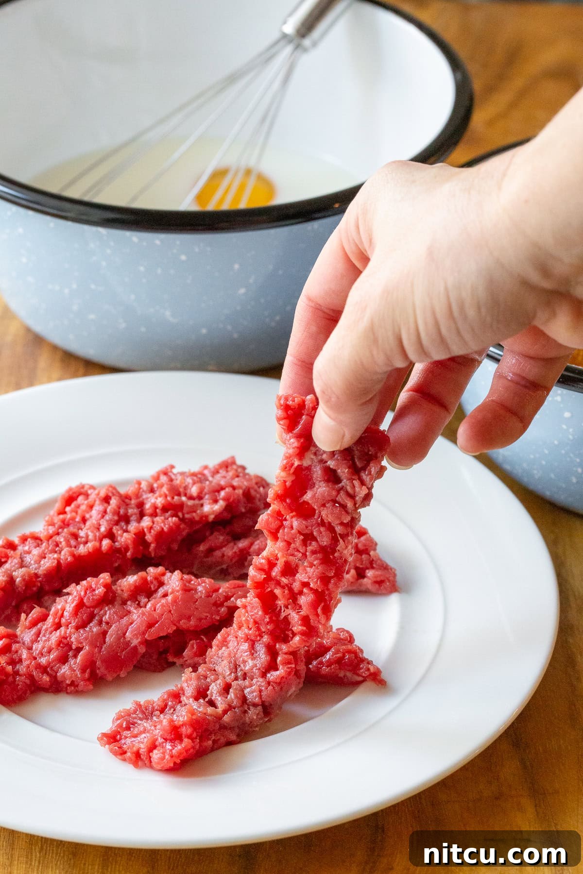 A hand holding a piece of raw cube steak before being breaded for steak fingers.