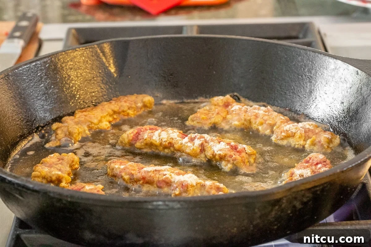 Several crispy steak fingers frying in a hot cast iron skillet, golden brown and bubbling.