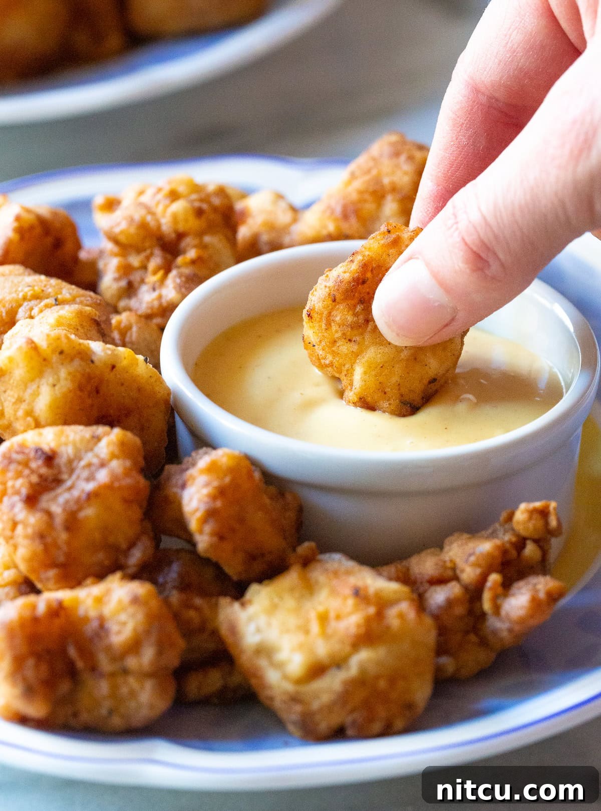 A hand dipping a crispy chicken nugget into a small white bowl of Chick-fil-A sauce.