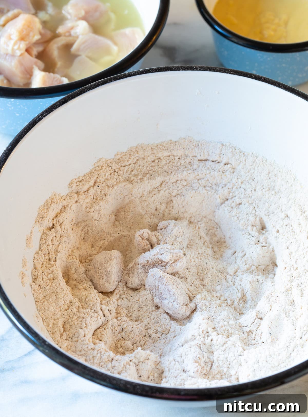 Bite-sized chicken chunks coated in the flour mixture, ready for frying.