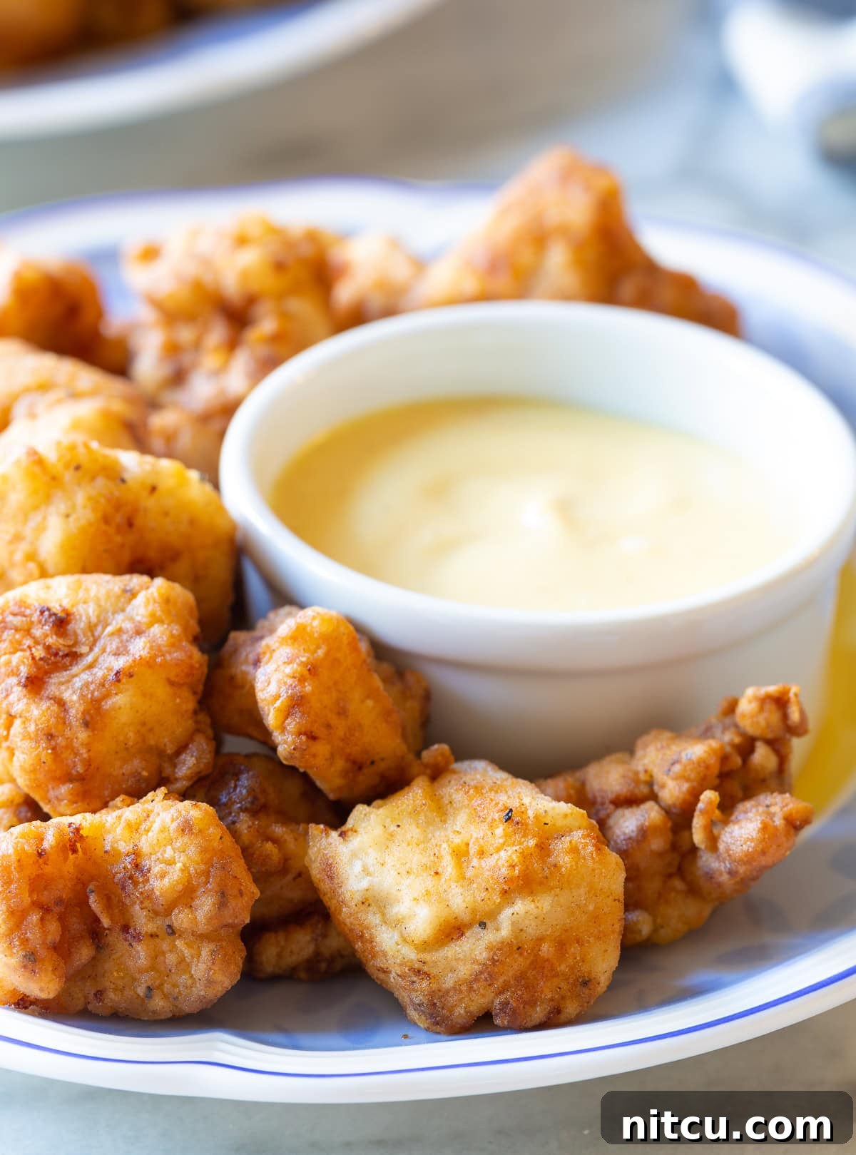 Crispy chicken nuggets arranged on a plate with a small bowl of copycat Chick-fil-A sauce in the center.