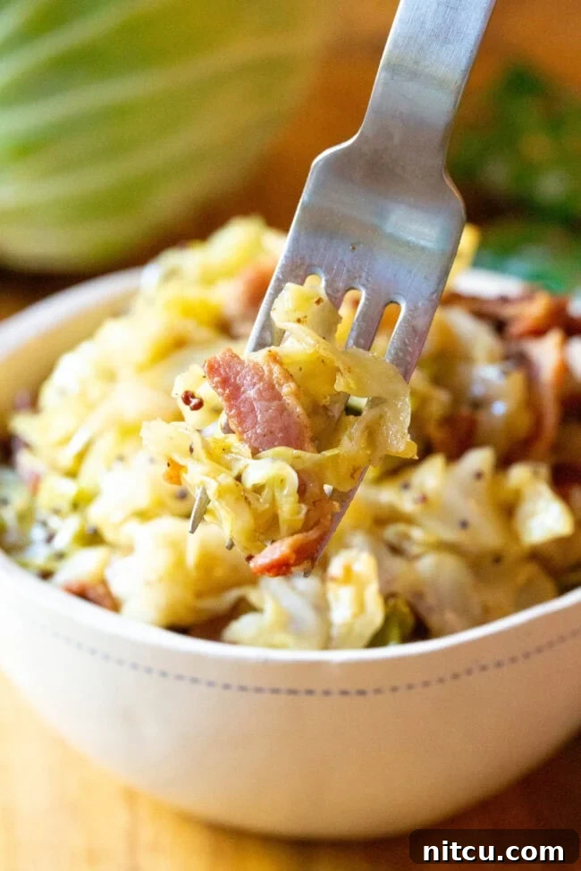 A serving of Irish Bacon and Cabbage in a white bowl with a fork taking a portion, showcasing its tender texture.