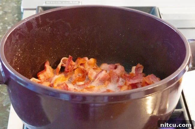 Diced bacon cooking in a large pot on a stovetop, rendering its fat.