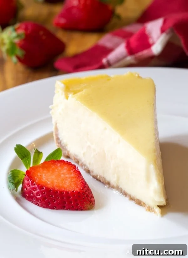 A beautifully sliced piece of Slow Cooker Cheesecake, garnished with a vibrant strawberry, presented on a pristine white plate. The cheesecake boasts a perfectly smooth, uncracked surface, highlighting its creamy texture.