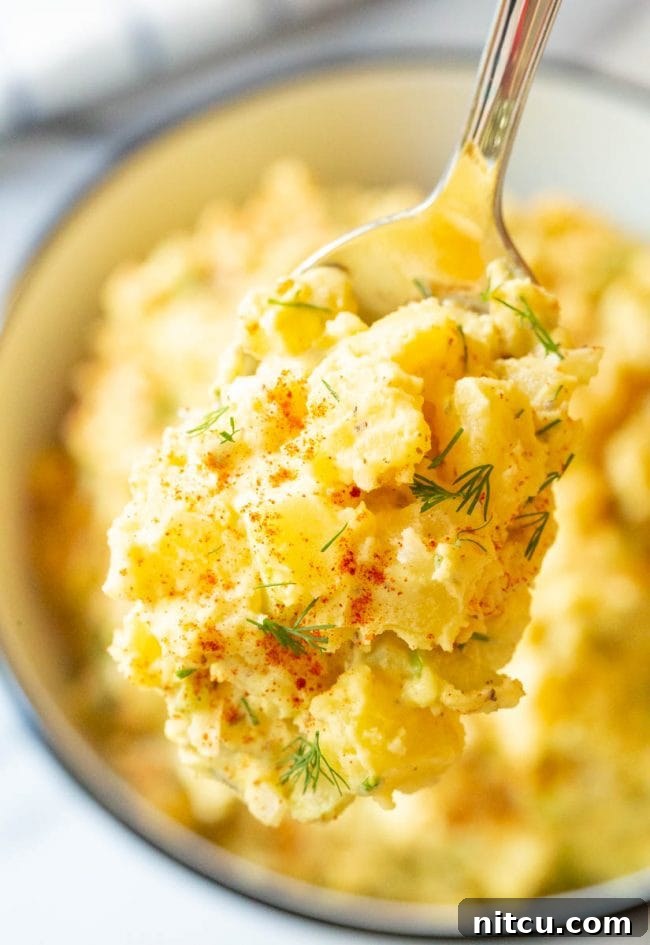 A close-up shot of a spoonful of creamy potato salad, revealing chunks of potato, egg, and vibrant relish.