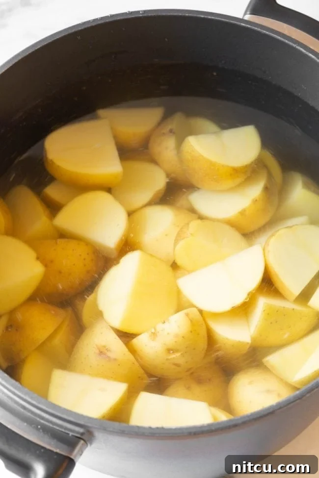 Potatoes boiling in a large sauce pot on the stove, ensuring even cooking.