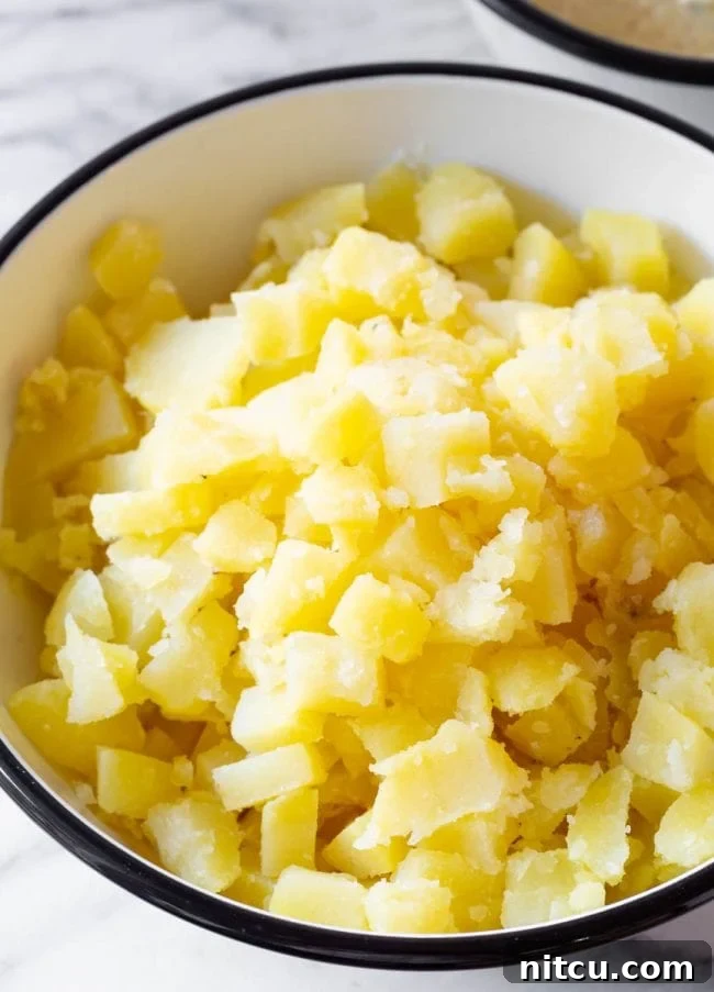 Close-up of cooked, peeled, and roughly chopped potatoes in a bowl, ready for the dressing.
