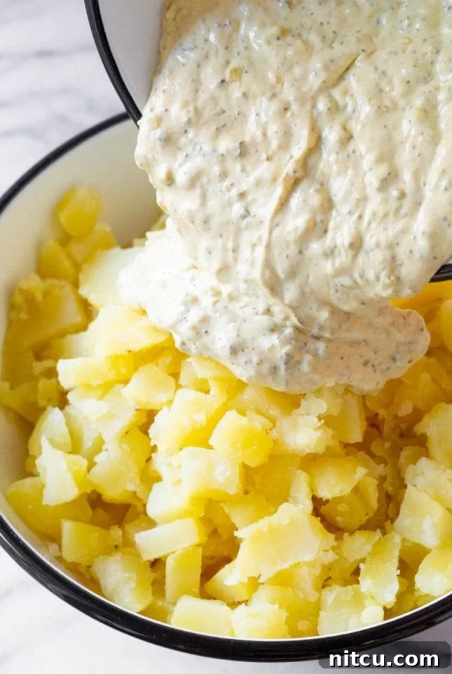 Creamy potato salad with dressing being poured over the cooked potatoes, ready for mixing.
