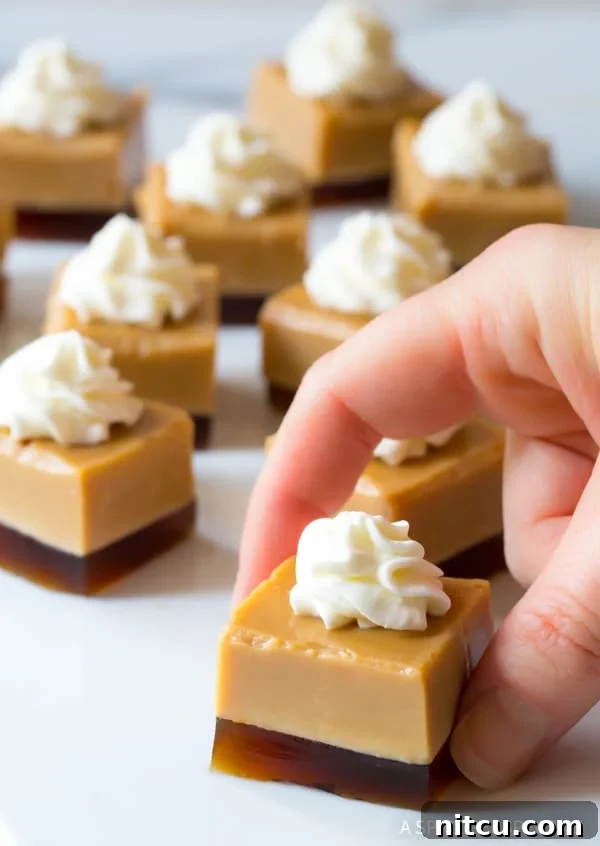 A hand holds a perfectly cut Baileys Irish Cream jello square, topped with a swirl of whipped cream, with more tempting shots in the background.