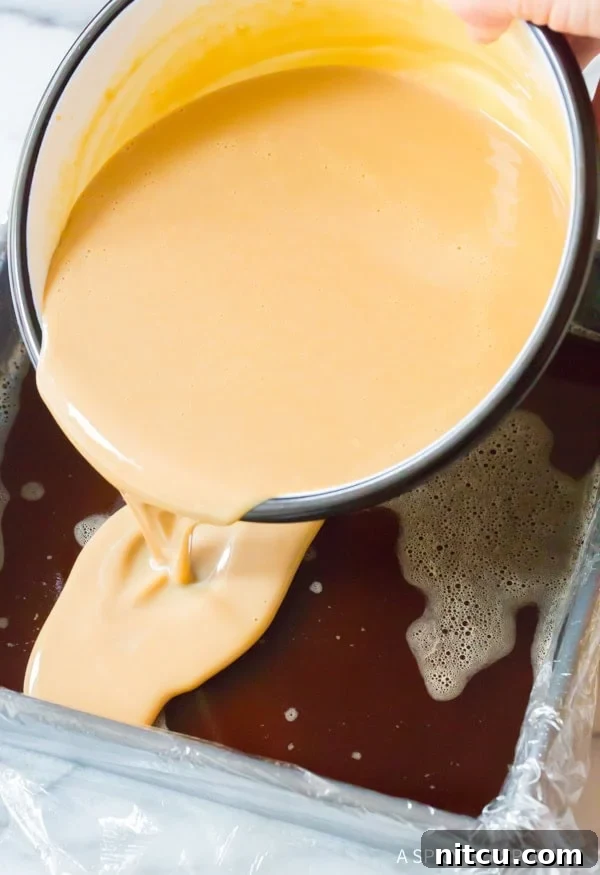 The creamy Baileys Irish Cream mixture being carefully poured over the set coffee layer in the baking dish, creating a beautiful two-toned effect.