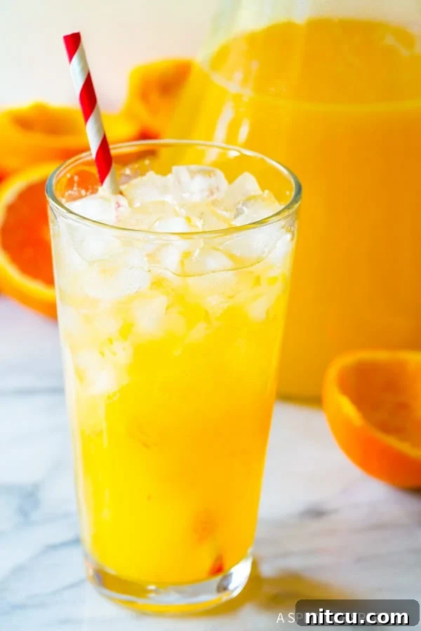 A tall pint glass filled with ice and fresh Orangeade, adorned with a red and white striped straw, ready for sipping.