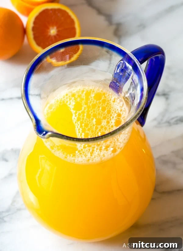 A large glass pitcher filled with homemade Southern orangeade, showcasing its bright, inviting color, ready to be served on a warm day.