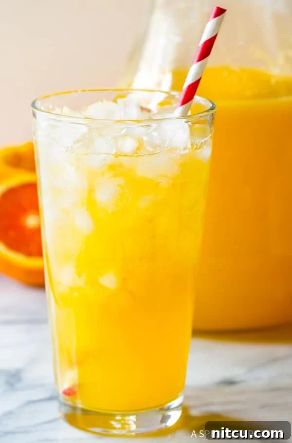 A close-up of a glass brimming with ice and homemade Southern orangeade, featuring a vibrant red and white striped straw, perfectly refreshing for summer.