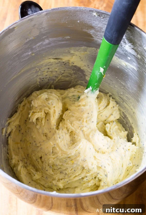 Lemon cookie dough being mixed in a stand mixer bowl with a rubber spatula.
