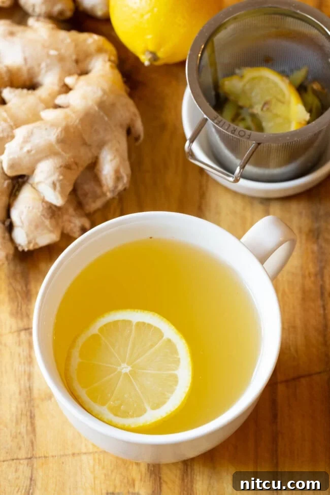 A close-up of a steaming cup of freshly made Lemon Ginger Detox Tea, showcasing the vibrant yellow lemon slices and grated ginger.