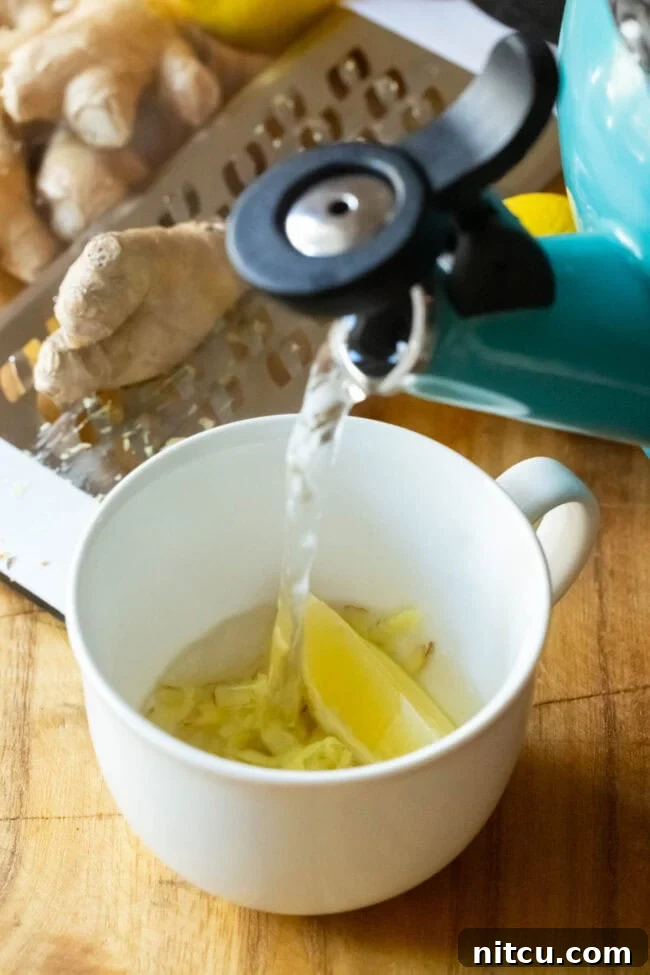 Steaming hot water being poured over the ginger and lemon in a mug, beginning the brewing process.