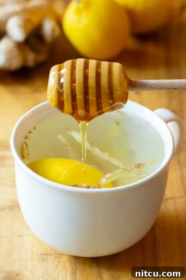 A drizzle of golden honey being added to the freshly brewed lemon ginger tea.
