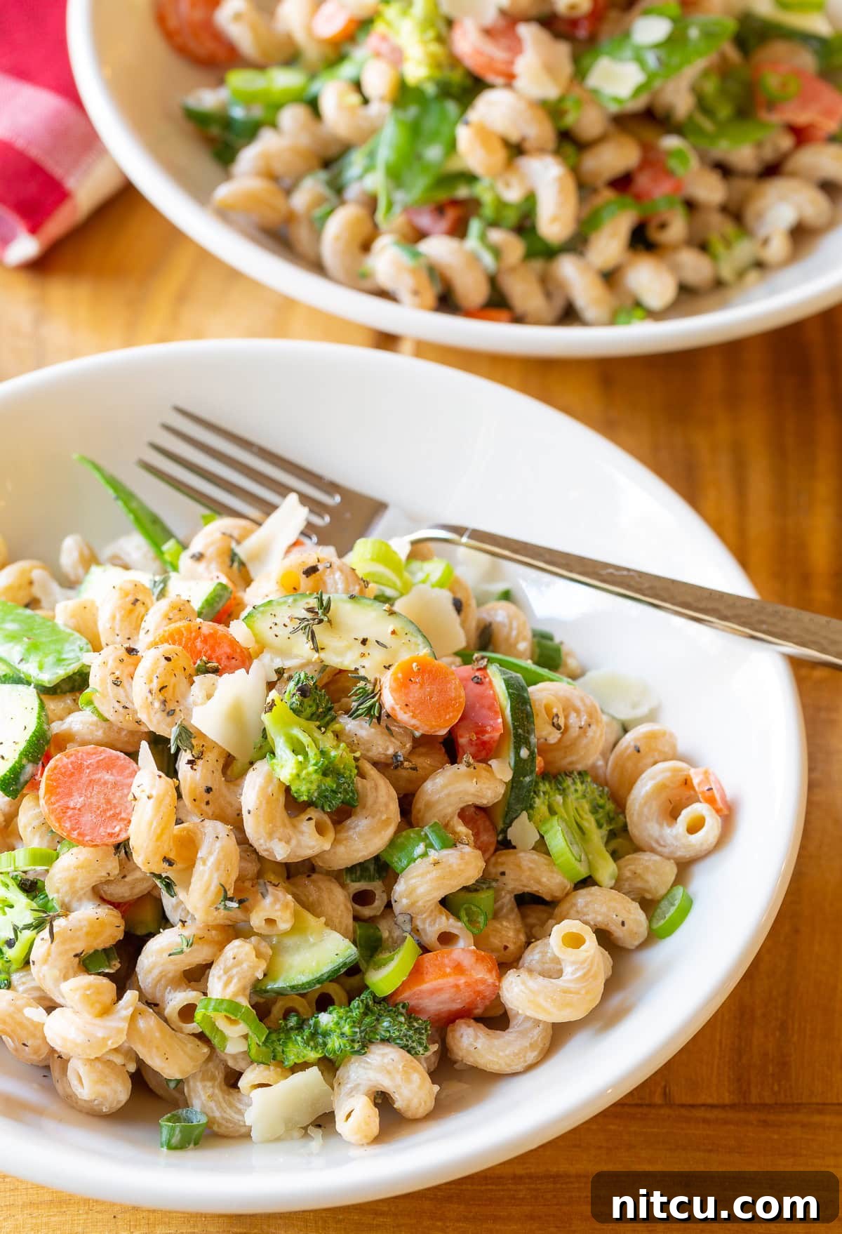 A close-up of a white bowl filled with skinny noodle primavera, showcasing finely chopped zucchini, carrots, broccoli florets, vibrant red peppers, and delicate shaved parmesan cheese.