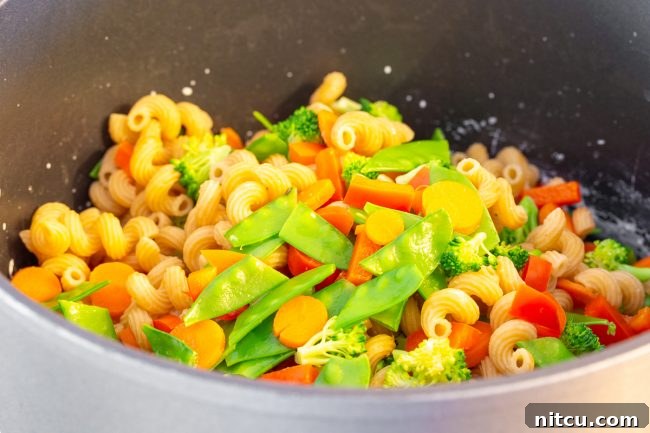 A large pot filled with drained pasta and blanched vegetables, ready for the sauce.