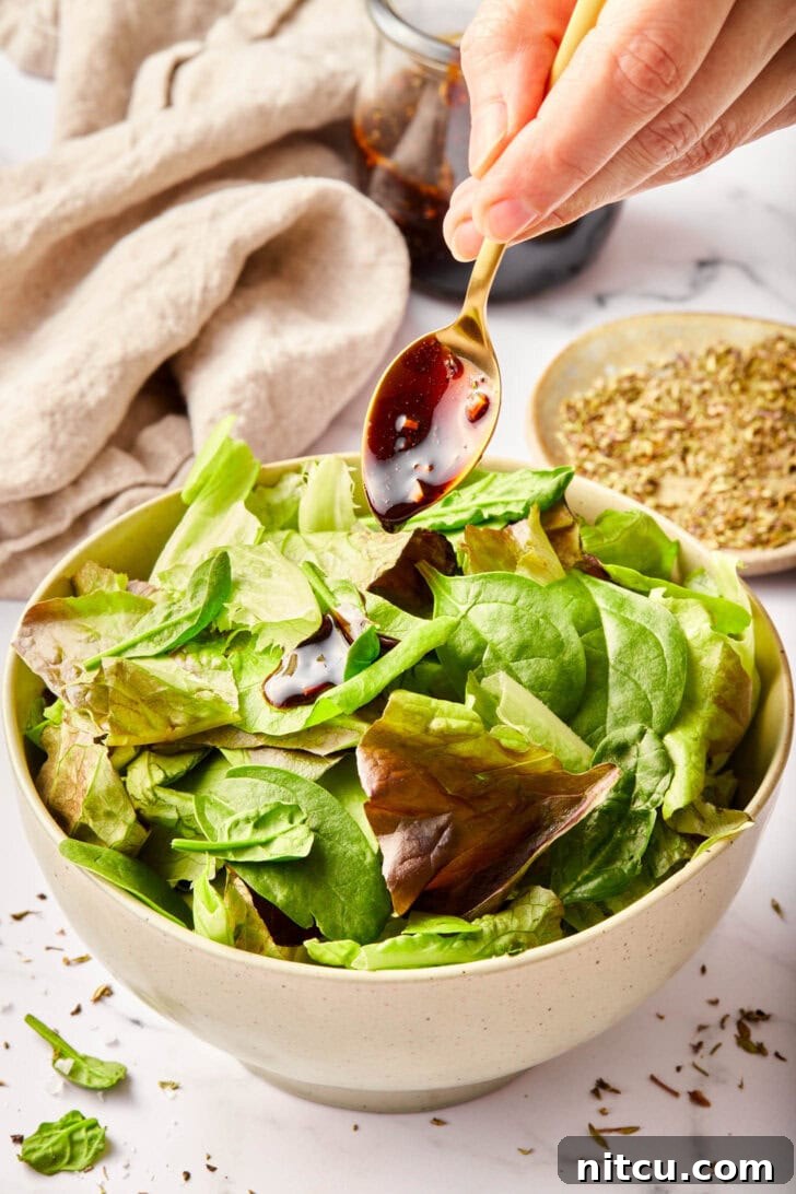 Homemade salad dressing with balsamic vinegar poured over greens.