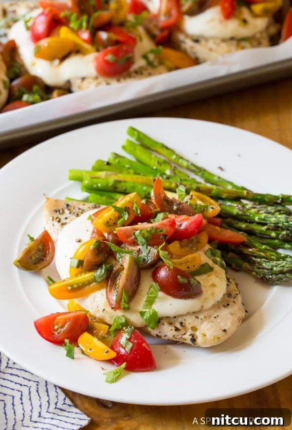 A close-up of a perfectly plated Cheesy Bruschetta Chicken, featuring the golden-brown chicken, melted cheese, and fresh tomato-basil topping, with roasted asparagus on the side, presented on a white plate.