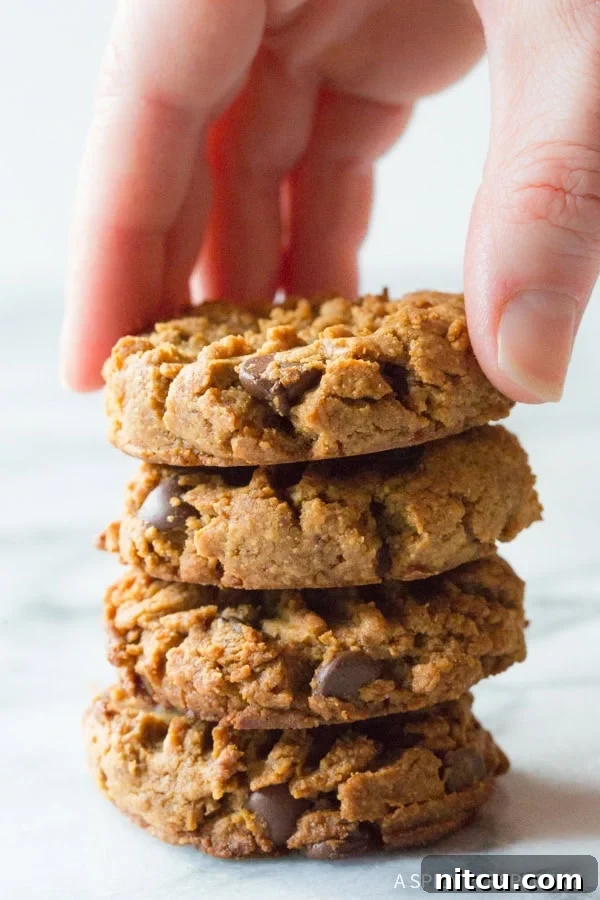 Hand reaching for a top cookie from a stack of four mouth-watering peanut butter chocolate chip cookies.