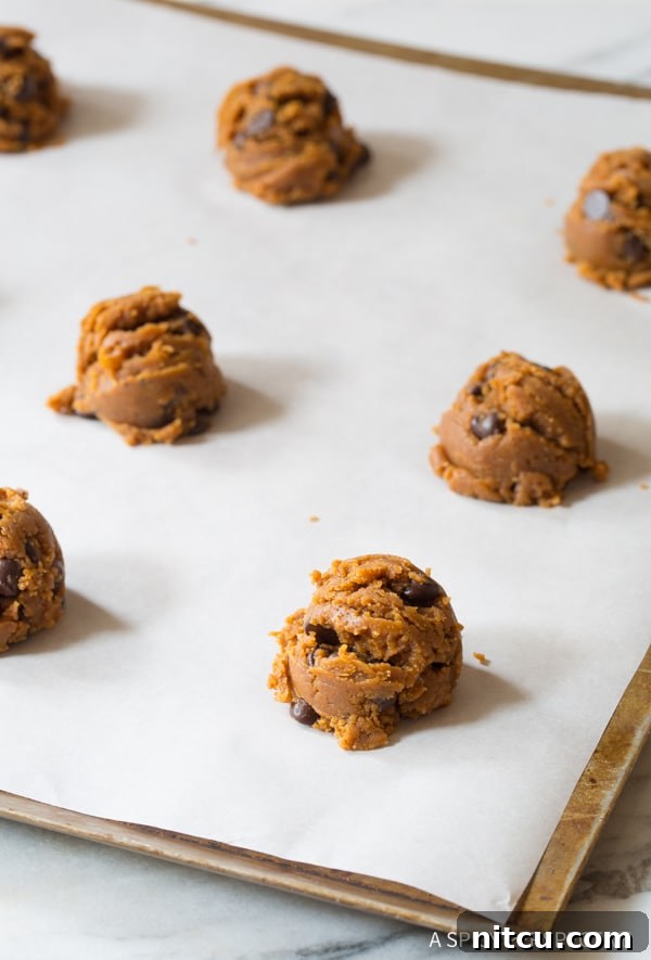 Perfectly round scoopfuls of raw cookie dough arranged on parchment paper on a baking sheet, ready for shaping.