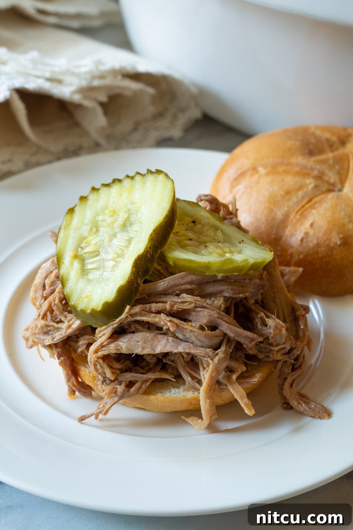 Shredded smoked pulled pork on a bun with pickles.