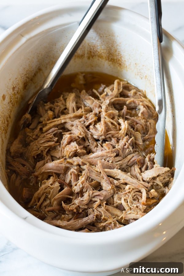 Shredded pork in the crockpot with metal tongs.