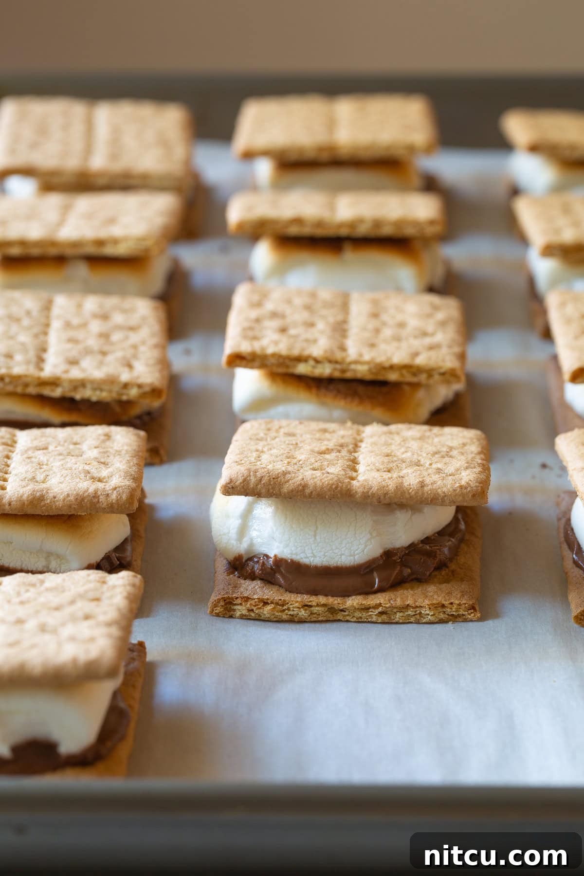 How To Make Smores In The Oven - Baked s'mores lined up on a baking sheet. 