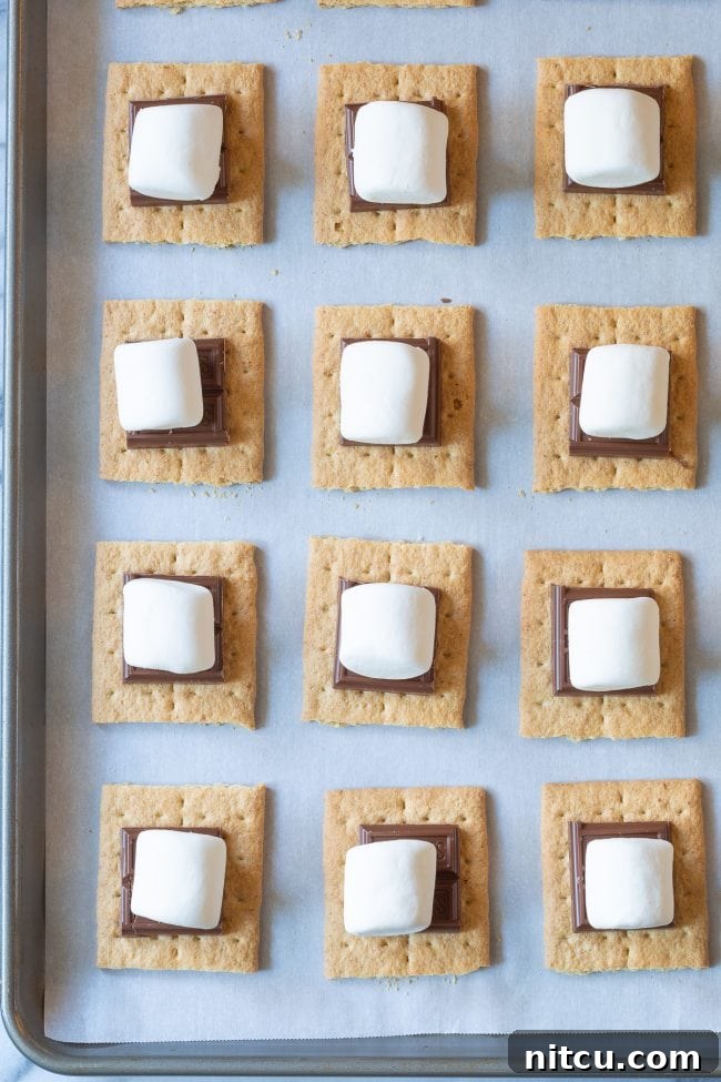 Overhead shot of graham crackers topped with chocolate and marshmallows before being broiled. 