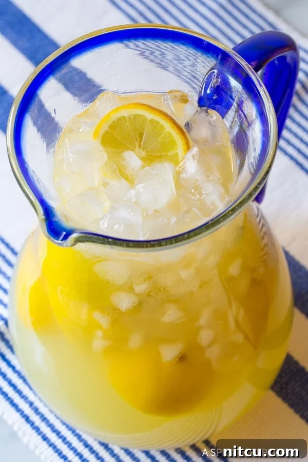 A large, clear pitcher of homemade Stevia Lemonade, brimming with ice and garnished with fresh lemon slices, perfectly chilled and ready to serve.