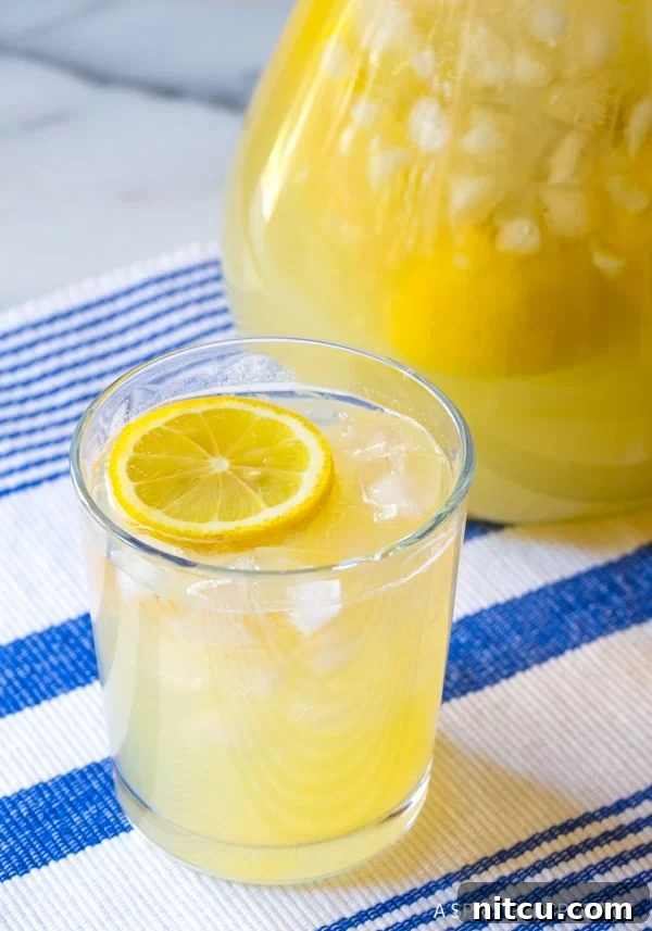 Close-up of a frosted glass filled with bright yellow stevia lemonade, brimming with ice and garnished with a fresh lemon slice, showing delightful condensation on the glass.