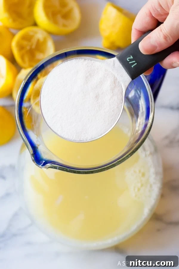A hand gently pouring powdered stevia sweetener into a pitcher of lemon juice, ensuring even distribution.
