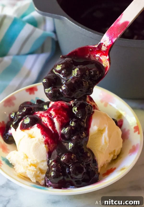 Spoon drizzling blueberry sauce over a bowl of vanilla ice cream.