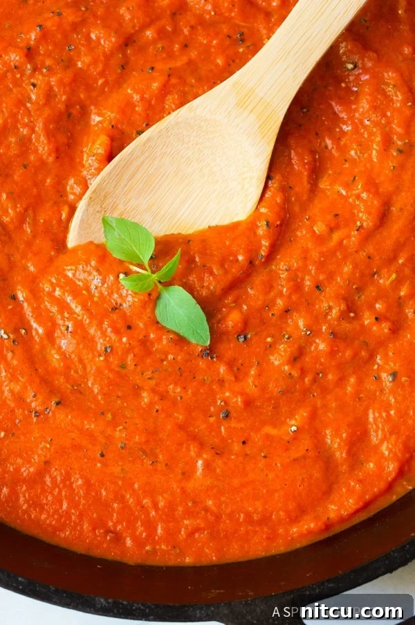 Roasted red pepper sauce with a wooden spoon and sprig of basil. 