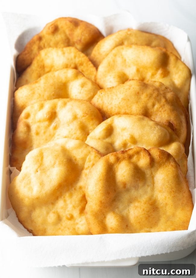 Freshly fried Navajo fry bread stacked neatly in a baking dish lined with paper towels, draining excess oil and ready to be served or topped.