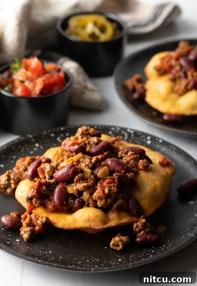 Delicious taco meat and red kidney beans artfully arranged on a crispy, golden fry bread base, preparing for further toppings.