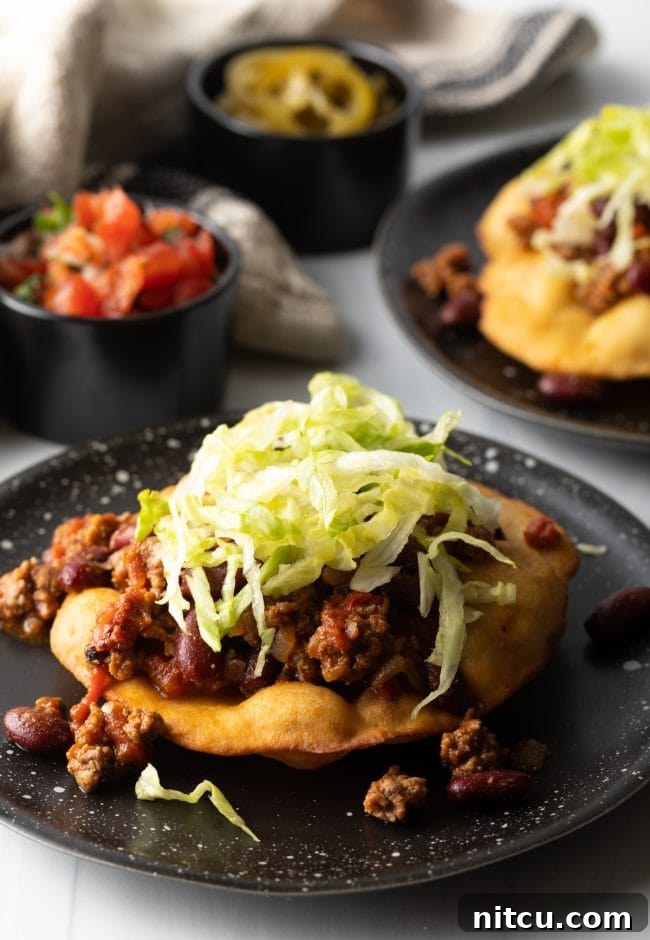 A hand assembling a crispy fry bread taco, layering seasoned meat and fresh shredded lettuce, preparing a delicious meal.