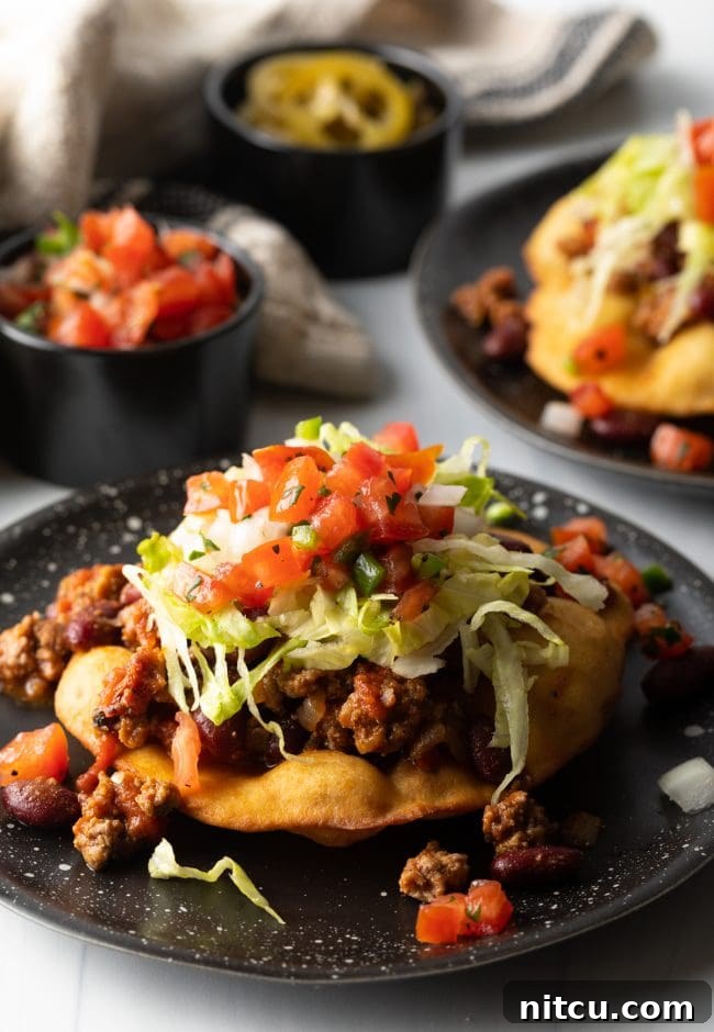 A fully loaded Navajo fry bread taco, generously topped with seasoned ground beef, fresh lettuce, tomatoes, and other vibrant garnishes, showcasing a hearty meal.