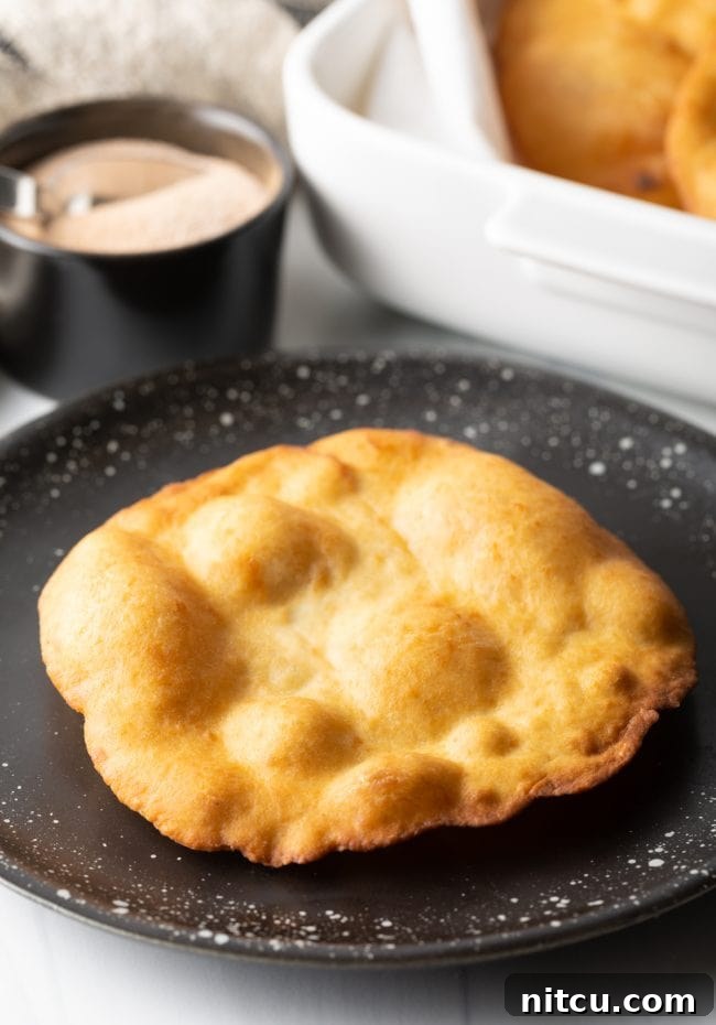 A freshly fried, golden-brown crispy fry bread resting on a black plate, showcasing its simple beauty before adding toppings.