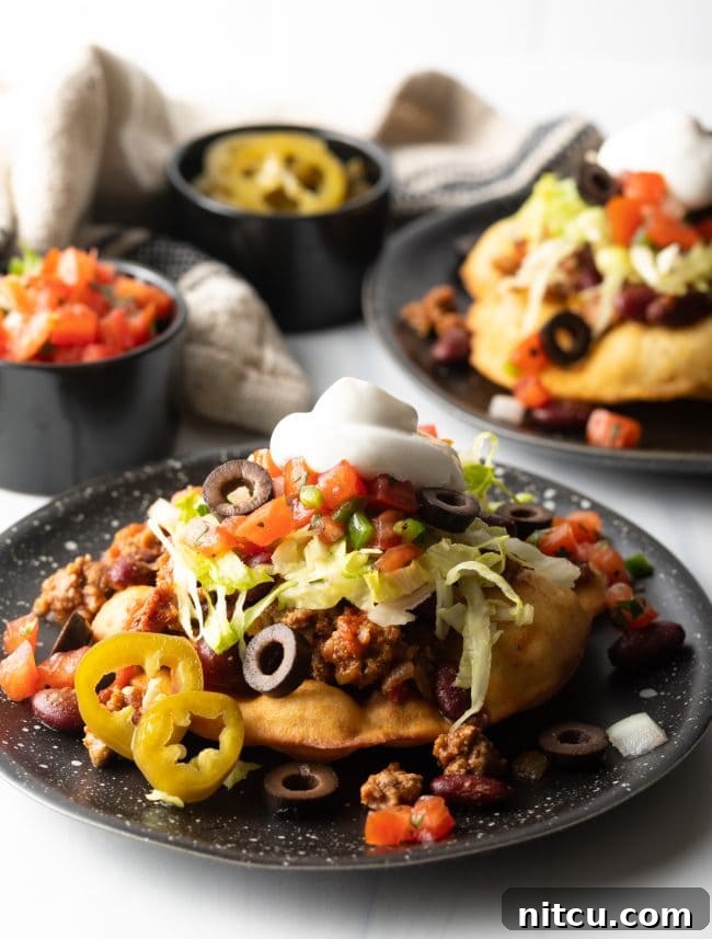 A beautifully arranged plate of Indian tacos, each topped with a generous portion of seasoned meat, fresh lettuce, and other colorful garnishes, ready to be enjoyed.