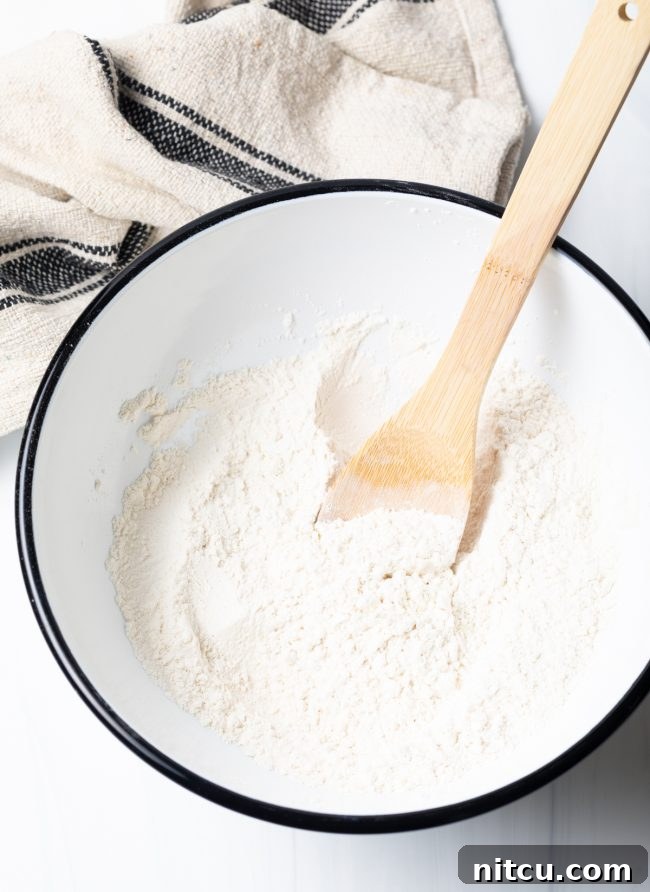 Dry ingredients for fry bread in a mixing bowl, ready to be combined, with a wooden spoon resting nearby.