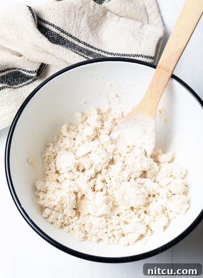 Fry bread dough being mixed vigorously with a wooden spoon in a sturdy mixing bowl, showing its developing consistency.