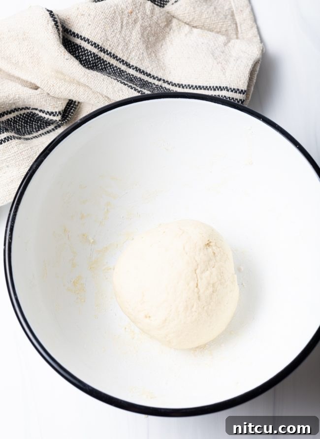 A perfectly formed ball of Navajo fry bread dough resting smoothly in a mixing bowl, covered and ready for its rest period.