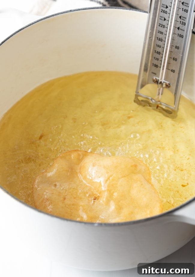 Tongs carefully flipping a piece of fry bread in the hot oil, revealing its golden-brown underside as it continues to cook evenly.